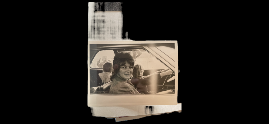 Vintage-Schwarzweißfoto einer lächelnden Frau auf dem Fahrersitz eines Autos mit zwei Kindern, eines neben ihr und eines auf dem Rücksitz.